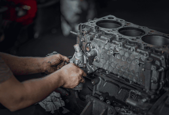 The mechanic at Hilltop Auto Diesel is working on a disassembled engine block, focusing on adjusting a component while wearing a short-sleeve shirt.