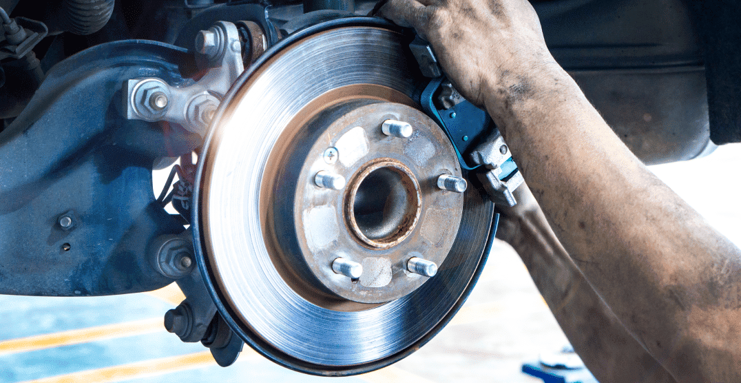 Mechanic working on a car's braking system, focusing on the brake disc and caliper with tools in hand, carefully ensuring proper brake fluid levels for optimal performance.