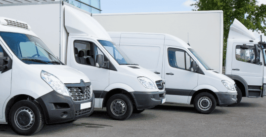 A row of white delivery vans and diesel trucks parked in a lot on a clear day, showcasing the efficiency of our fleet management services.